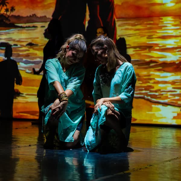 Duo de danseuses en tuniques turquoise devant un décor de coucher de soleil