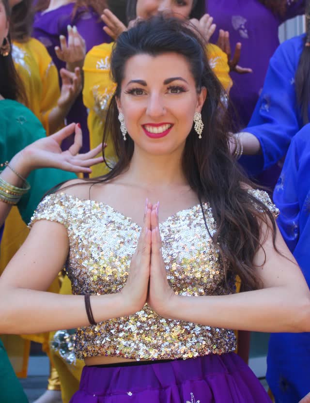 Danseuse saluant les mains jointes, entourée de son groupe en tenues colorées